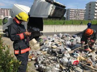 収集車の荷台の扉が開けられ、沢山のゴミが出されており、消防服を着た職員の方がゴミの中に入って棒を持って作業をしている写真