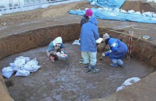 遺構の中で、小さなスコップなどを使い土の掘削を行っている4名の作業者の写真