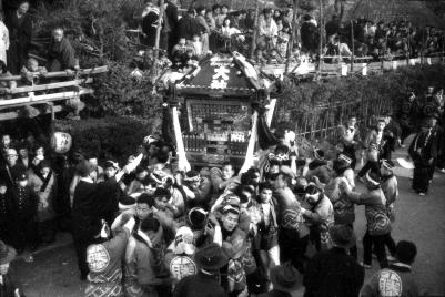 法被を着た多くの男性が二宮神社神輿を担いでおり、多くの観客で賑わっている様子の白黒写真