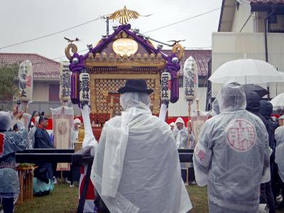 傘やカッパを着た人々が二宮神社の神輿の周りに集まっている様子の写真