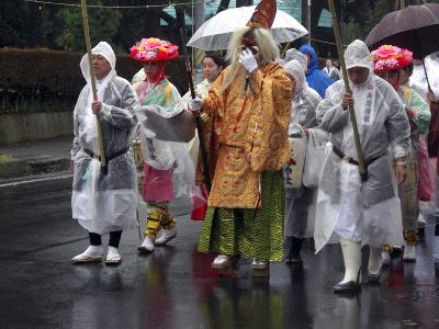 猿田彦命の格好をした方を先頭に、花笠を被った人やカッパや傘を差した人が歩いている様子の写真
