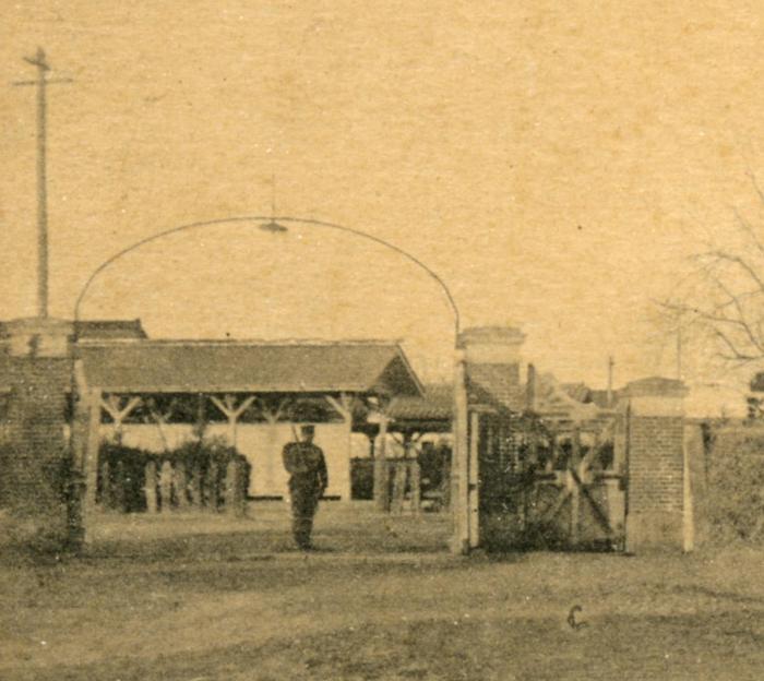 表門前に1人の兵士が立っている連隊敷地内を南側から写したセピア色の写真