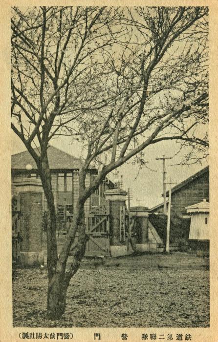 大きな1本の木や建物などがある鉄道第二連隊を営門前から写したセピア色の風景写真