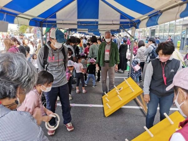 市民まつりのテントで輪投げに挑戦する子供と、それを見守る親