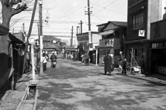 商店や住宅が密集しており、中央奥に京成線の踏切がある白黒写真