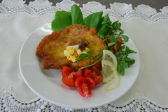 緑の野菜、トマトやレモンのスライスなどが一緒にお皿に盛りつけられたシュニッツェル（ドイツ風カツレツ）の写真