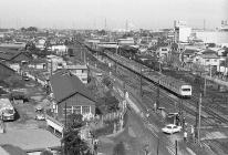 住宅や大きな建物が建ち並び、線路を列車が走っている様子を上から写した白黒写真