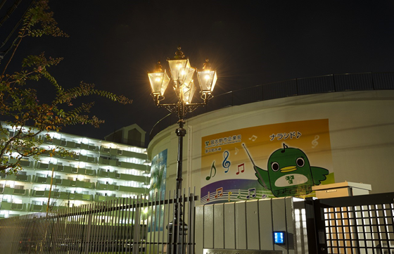 ナラシド♪のイラストが描かれたタンクのある第4給水場に設置されている5灯式のガス灯が夜道をやさしく照らしている写真