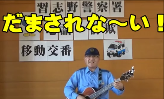 「だまされな～い！」と書かれている文字の下に警察官がギターを持ち歌っている写真