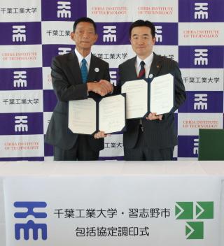 左手に協定書を持ち、右手で握手をしている瀬戸熊理事長と宮本市長の記念写真