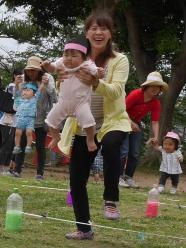 ピンク色の鉢巻きを巻いた子供と子供を抱えた母親がジャンプしている様子の写真