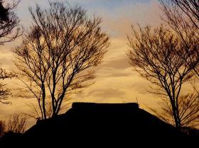 周辺に木々が立つ一軒家に日が沈み茜色に染まる空を写した原風景写真