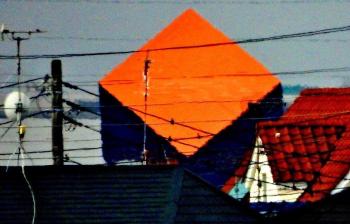 住宅街の民家の屋根にオレンジ色の隕石が突き刺さったように見える商業施設の異形広告塔の写真