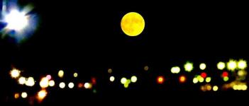 暗闇に浮かぶ複数の夜景のライトと夜空に浮かぶ黄色い満月を写した写真