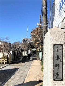 手前右側に「薬師寺」と書かれた石柱があり、左側に門へと続く石畳の道が伸びている写真
