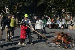 広場の一角、薪に火を焚き、長い棒を持っている女の子と男性の写真