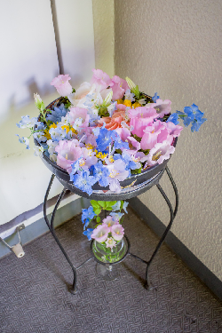 薄いピンク色や青色の花を浮かべた2週間目の花手水の器が玄関隅に置かれている写真