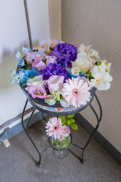 紫色や白色や薄いピンク色の花を浮かべた3週間目の花手水の器が隅に置かれている写真