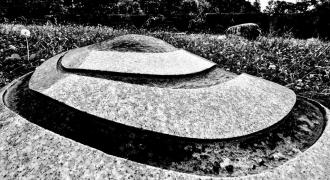 垣根を背景に、渦巻き型になっている丸い大きな石の白黒写真