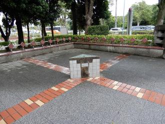 広場の一角に十字に茶色のタイルが敷かれ、十字が交差する部分に長崎モニュメントが設置されている写真