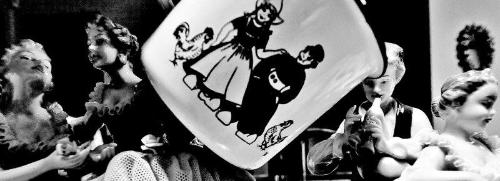 藤崎にある、西洋風の人形、女の子と男の子と鶏が描かれたカップが写されたディスプレイの白黒写真