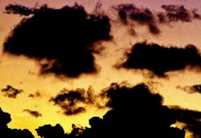 朝日で薄いオレンジ色に染まった空に黒い雲が浮かんでいる写真