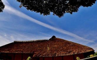 茅葺屋根の上に白い一筋の雲が伸びている写真