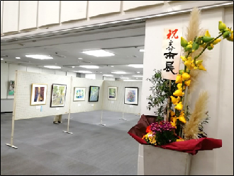 展示室入口に生け花が置かれ、奥のパネルに写真が展示されている写真