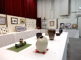 白い布が掛けられた台の上に、花瓶などの陶器が展示されている写真