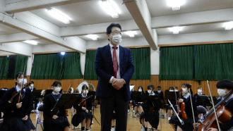 オーケストラ部の前で両手を組んで立ち挨拶をしている山岡先生の写真
