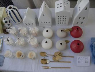 白い家の形の置物、花瓶、キャンドル、スプーンやフォークなどの雑貨が並べて置かれている写真