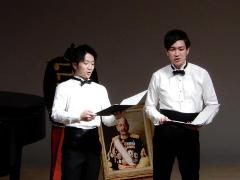 蝶ネクタイを付けた男子学生2名が手に楽譜を持ち千葉県一周唱歌を歌っている写真