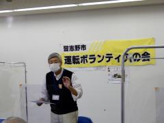 「習志野市運転ボランティアの会」と書かれた黄色い横断幕の前で話をしている 畑中会長の写真