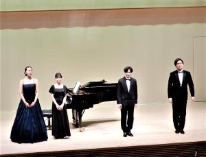 舞台の中央にグランドピアノがありその前に立つ韓国民謡歌唱・井出さん、ピアノ石井さん、宮田さん、喜久田さんの写真