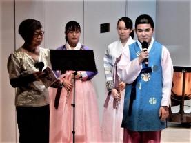 北村まさる合唱部部長が韓国の民族衣装を着て挨拶をし、その周りに3名の人が立っている写真