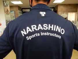 紺色のシャツの背中にNARASHINO Sports Instructorsとプリントされている写真