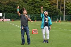 フィールド内で右手を上にあげ応援をしている佐藤さんと織戸団長の写真