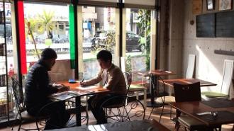 大きな窓の前のテーブルで2名の人が向かい合わせに座り話をしている写真