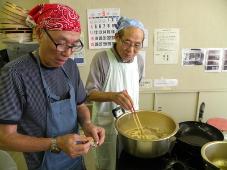 男性2名で鍋を使い料理をしている写真