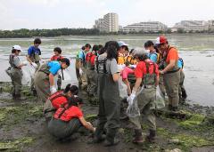 干潟の地面にいる生き物を観察している長靴を履いてオーバーオールの作業服を着た参加者の方々の写真