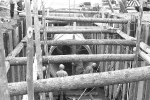 丸太で枠組みされた奥でヒューム管を設置している作業員達の白黒写真