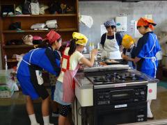こども料理教室で三角巾を付けた子供たちが調理を行っている様子の写真