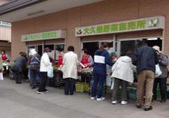 大久保野菜直売所と書かれた入口前の直売所にたくさんの買い物客が並んで買い物をしている写真