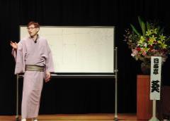 ステージ上に落語家で理学療法士の資格をもつ日向亭葵さんが講演を行っている様子の写真