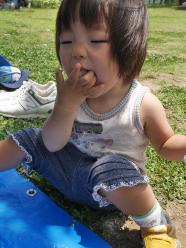 外で小さな子供が座りながら手で食べ物を食べている様子の写真