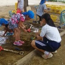 砂場で遊ぶ園児と女子中学生の写真