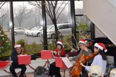 クリスマスの赤と白の帽子を被り、バイオリンなどの楽器を使い演奏している写真