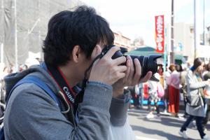 町ゆく人々を男性が一眼レフカメラで撮影している横顔を写した写真