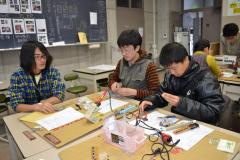 机の上で学生の指導を受けながら電子部品を組み立てている写真