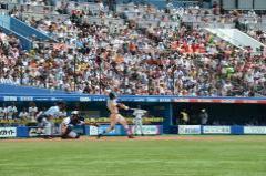 打席に立ちバットを振る習志野高校の選手、キャッチャー、球審と奥に映る観客席を1塁側から写した写真